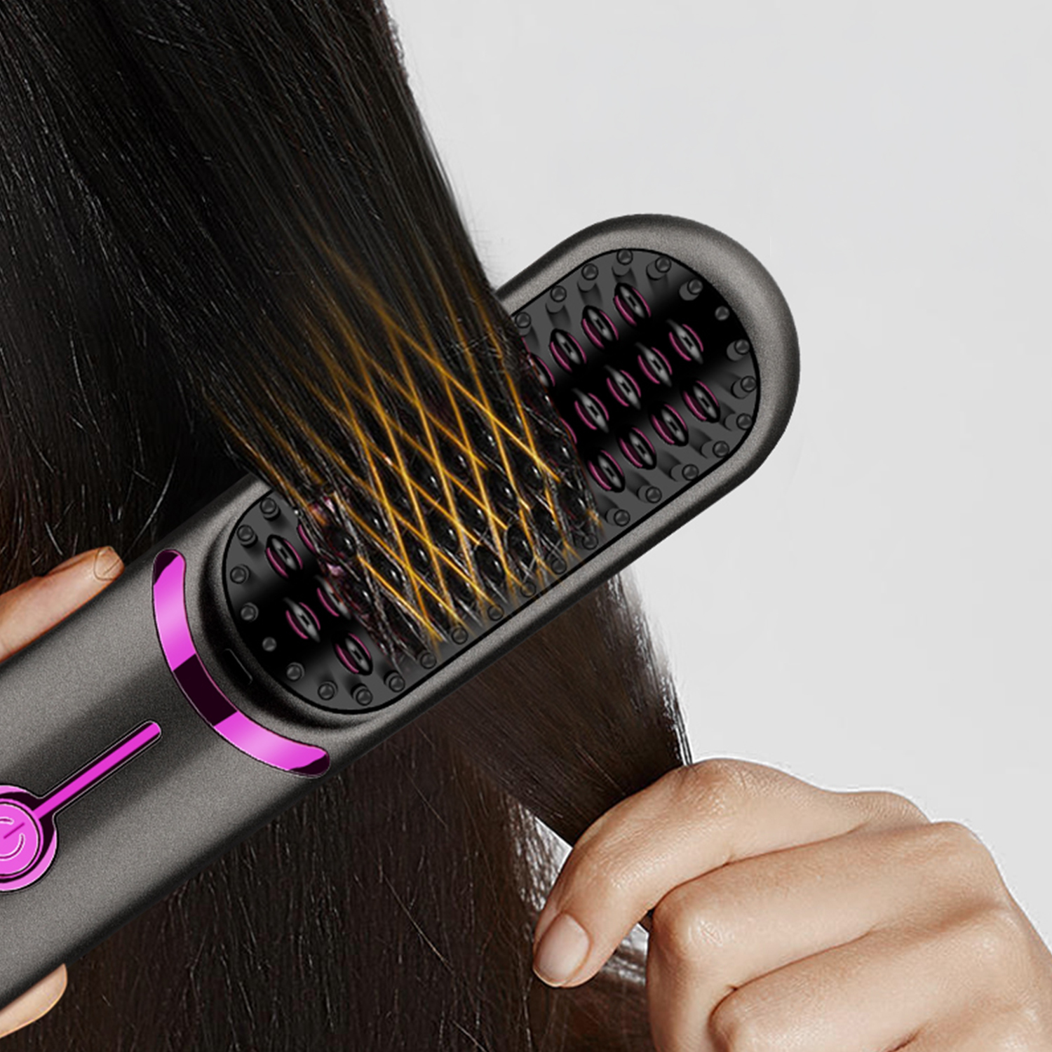 Una mano alisa el cabello oscuro usando un cepillo alisador negro y rosa contra un fondo gris.