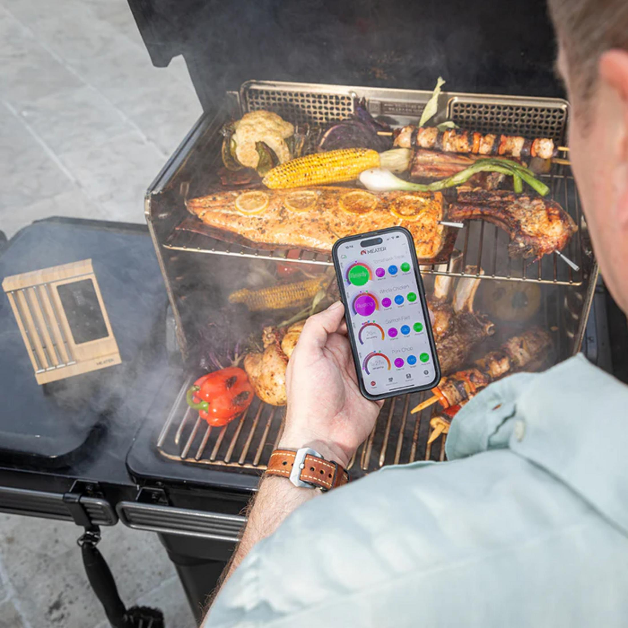 Un homme utilise une application mobile avec des données de température pour surveiller divers aliments au grill.