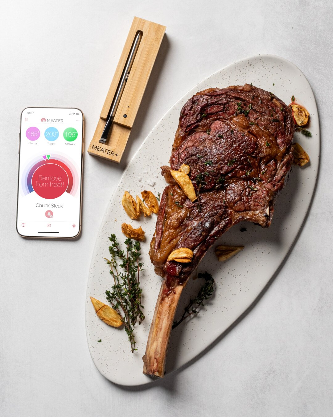 Steak tomahawk grillé sur plateau avec herbes, thermomètre et application de cuisson.