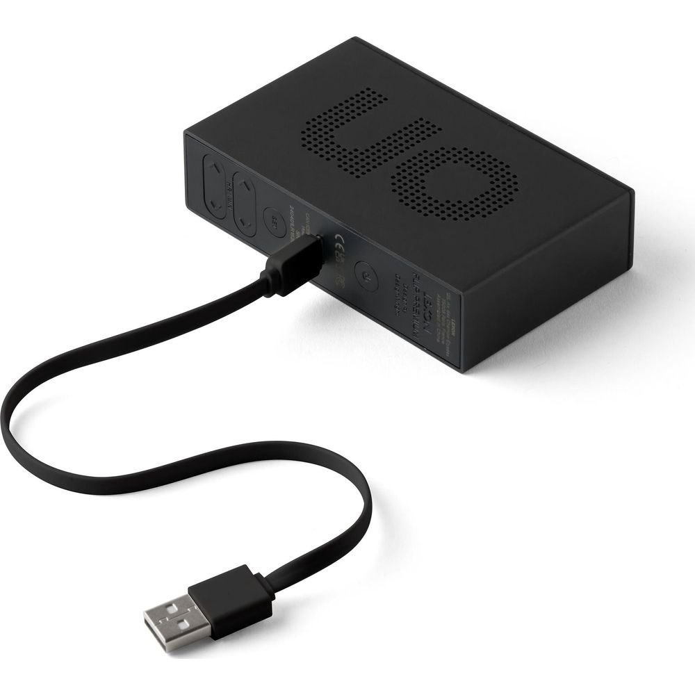 Ein schwarzes, rechteckiges elektronisches Gerät mit perforiertem Lautsprechergitter und angeschlossenem USB-Kabel.