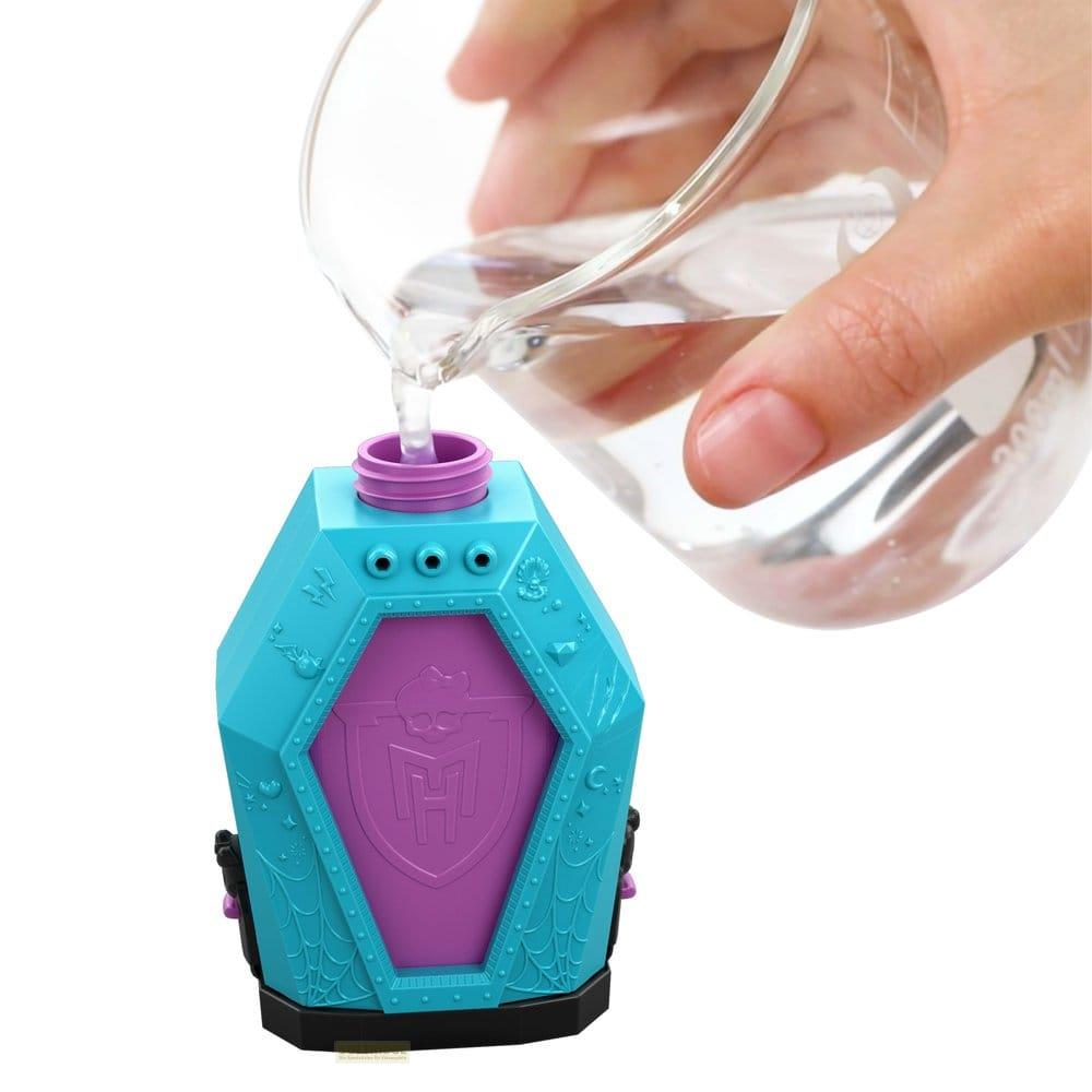 Wasser wird aus einem Glasbecher in einen blau-violetten sargförmigen Behälter gegossen.