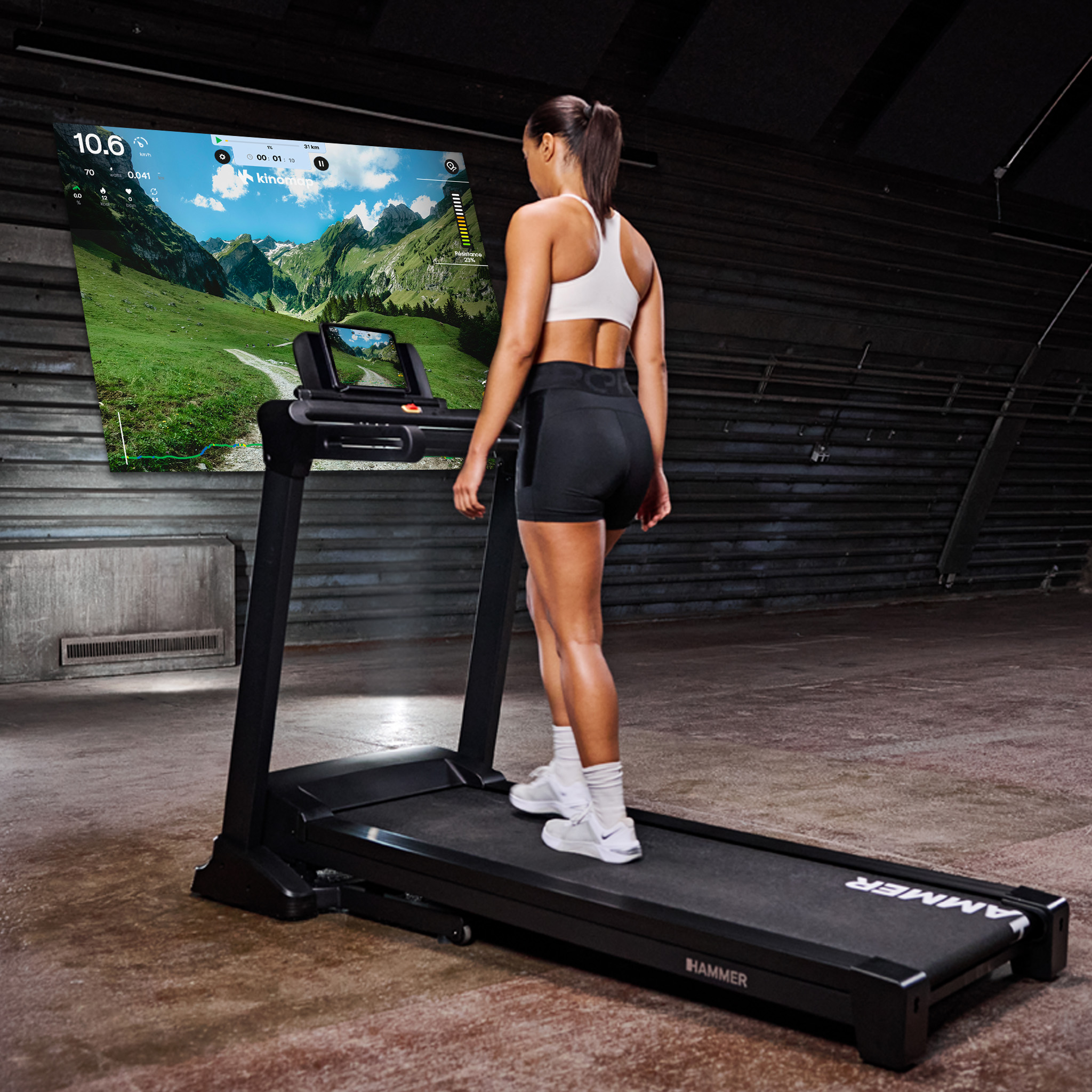 Eine Frau in Sportkleidung läuft auf einem Laufband vor einer großen Berglandschaft-Projektion.