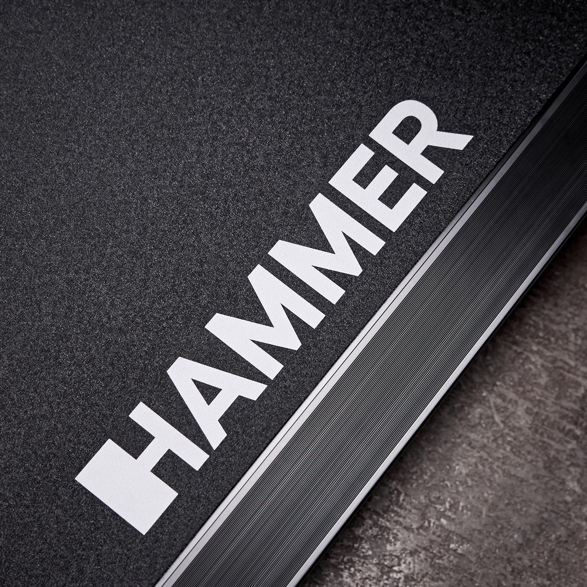 Nahaufnahme einer schwarzen strukturierten Oberfläche mit dem weißen Text HAMMER und einer Metallkante.