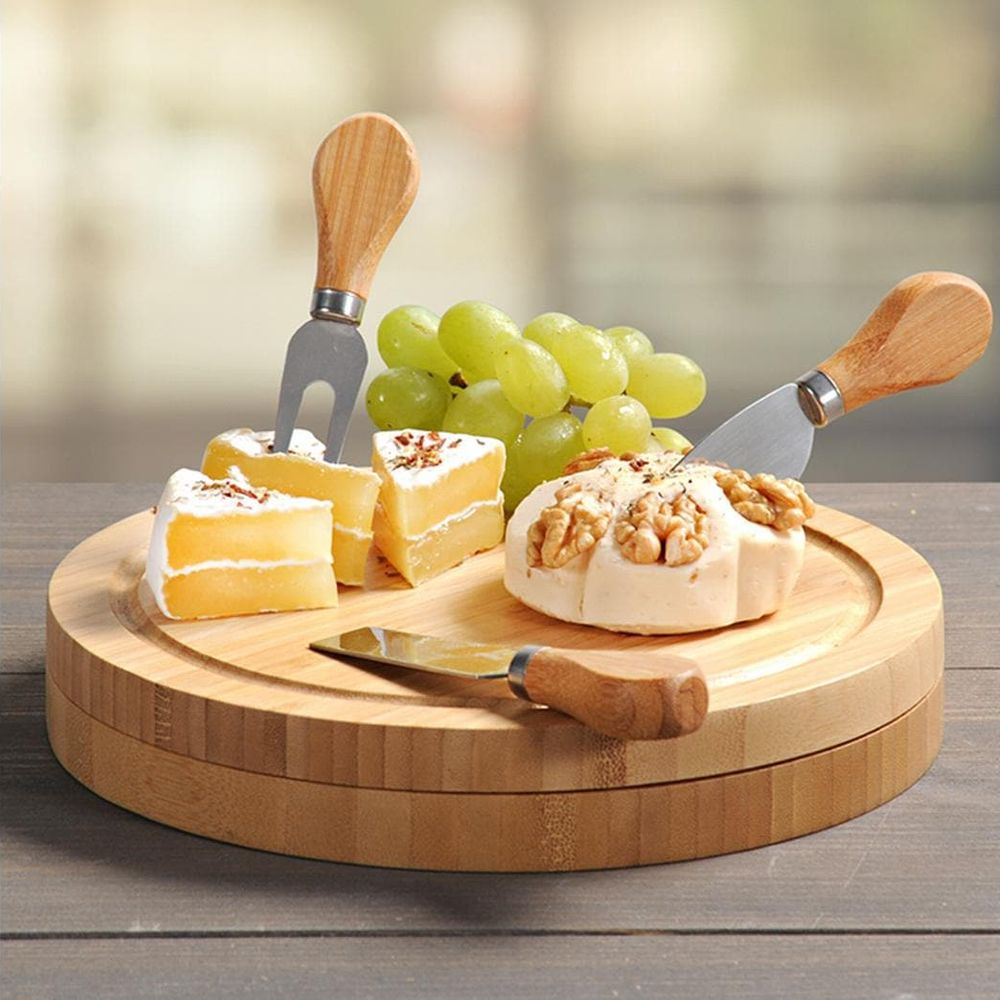 Käse und Weintrauben auf einem runden Holzbrett mit drei Messern.