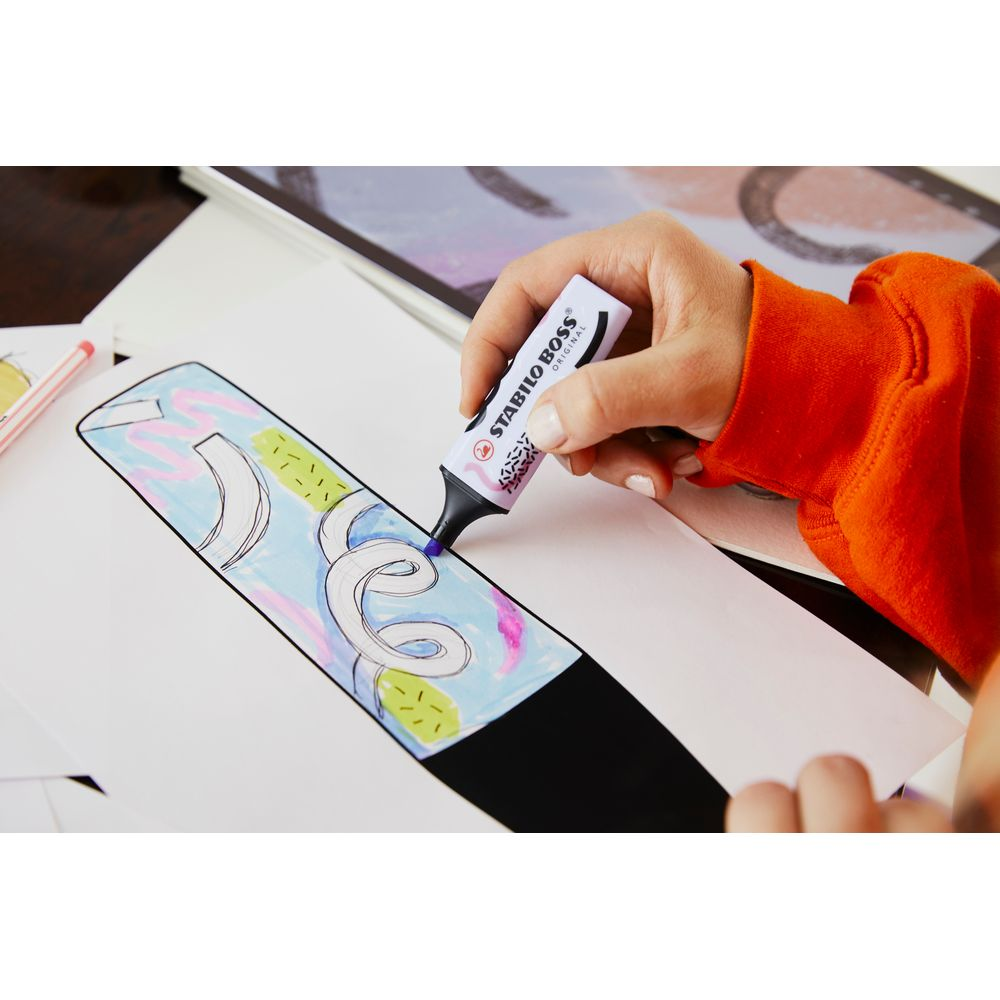 Eine Hand im orangefarbenen Pullover nutzt einen Stabilo Boss Textmarker, um auf Papier zu zeichnen.