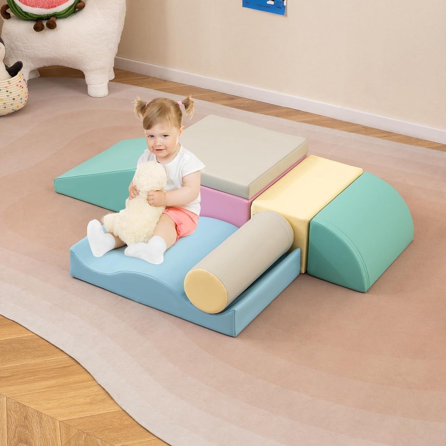 Un tout-petit tient une peluche assis sur des blocs de mousse souple colorés sur un tapis.