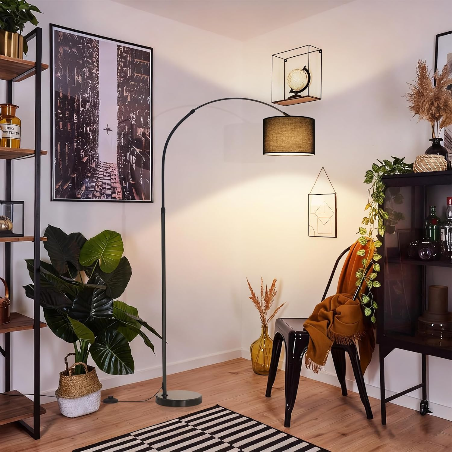 Eine schwarze Bogenlampe beleuchtet eine gemütliche Ecke mit Pflanzen, einem schwarzen Stuhl und einem Stadtposter.