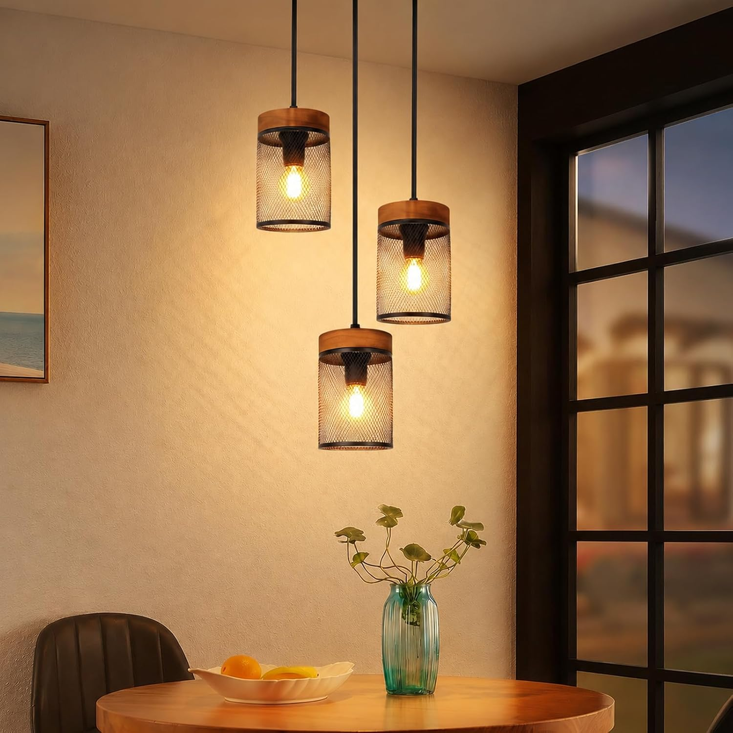 Drei hängende Lampen über einem Tisch mit einer Vase und Früchten, neben einem Fenster.