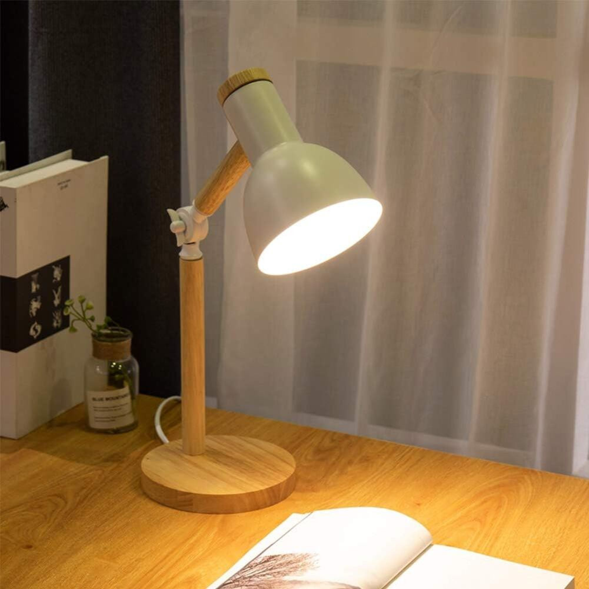 Eine weiße und holzfarbene Schreibtischlampe leuchtet auf einem Holztisch, daneben ein Buch.