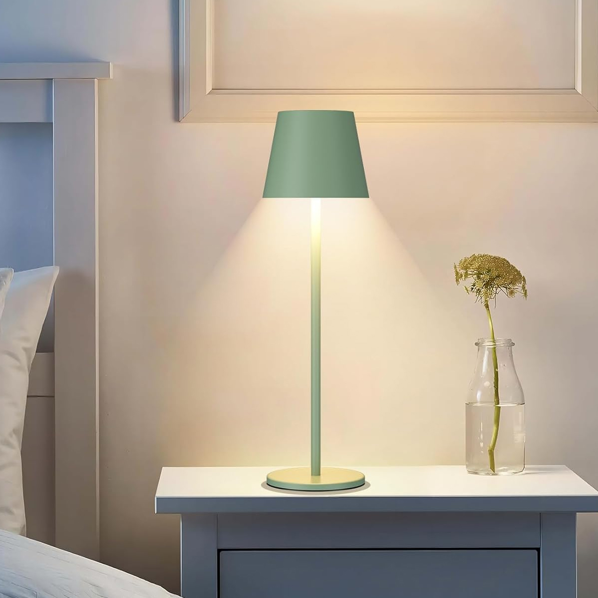 Eine moderne grüne Schreibtischlampe auf einem weißen Nachttisch neben einer Vase in einem Schlafzimmer.