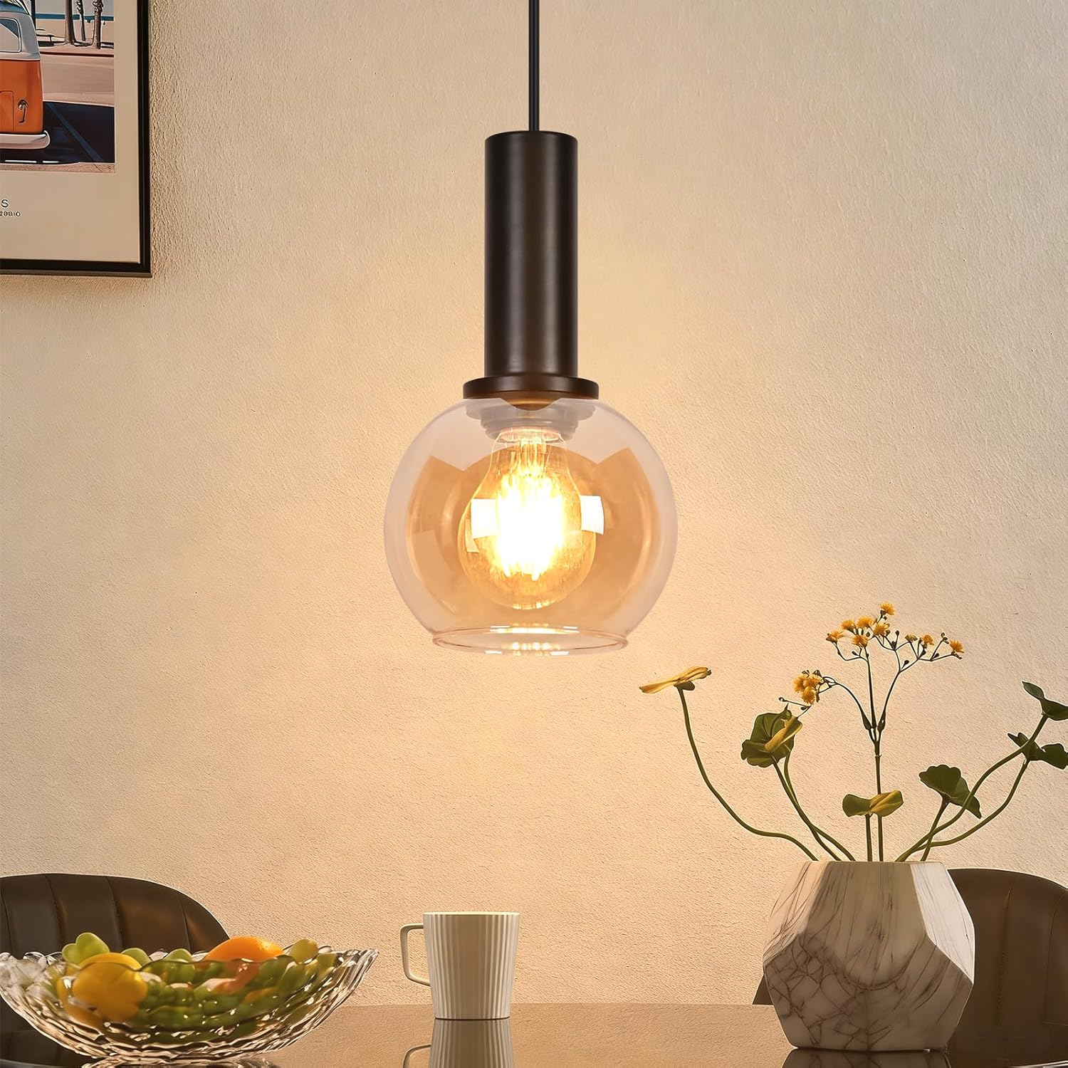 Eine schwarze Hängeleuchte mit Glasballon beleuchtet einen Tisch mit Obstschale, Tasse und Vase.