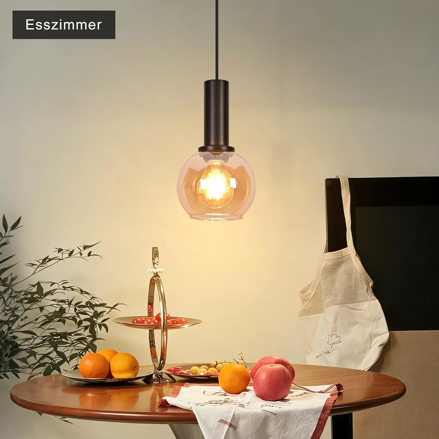 Hängelampe über einem Holztisch mit frischem Obst, einer Serviette und Pflanzen im Hintergrund.