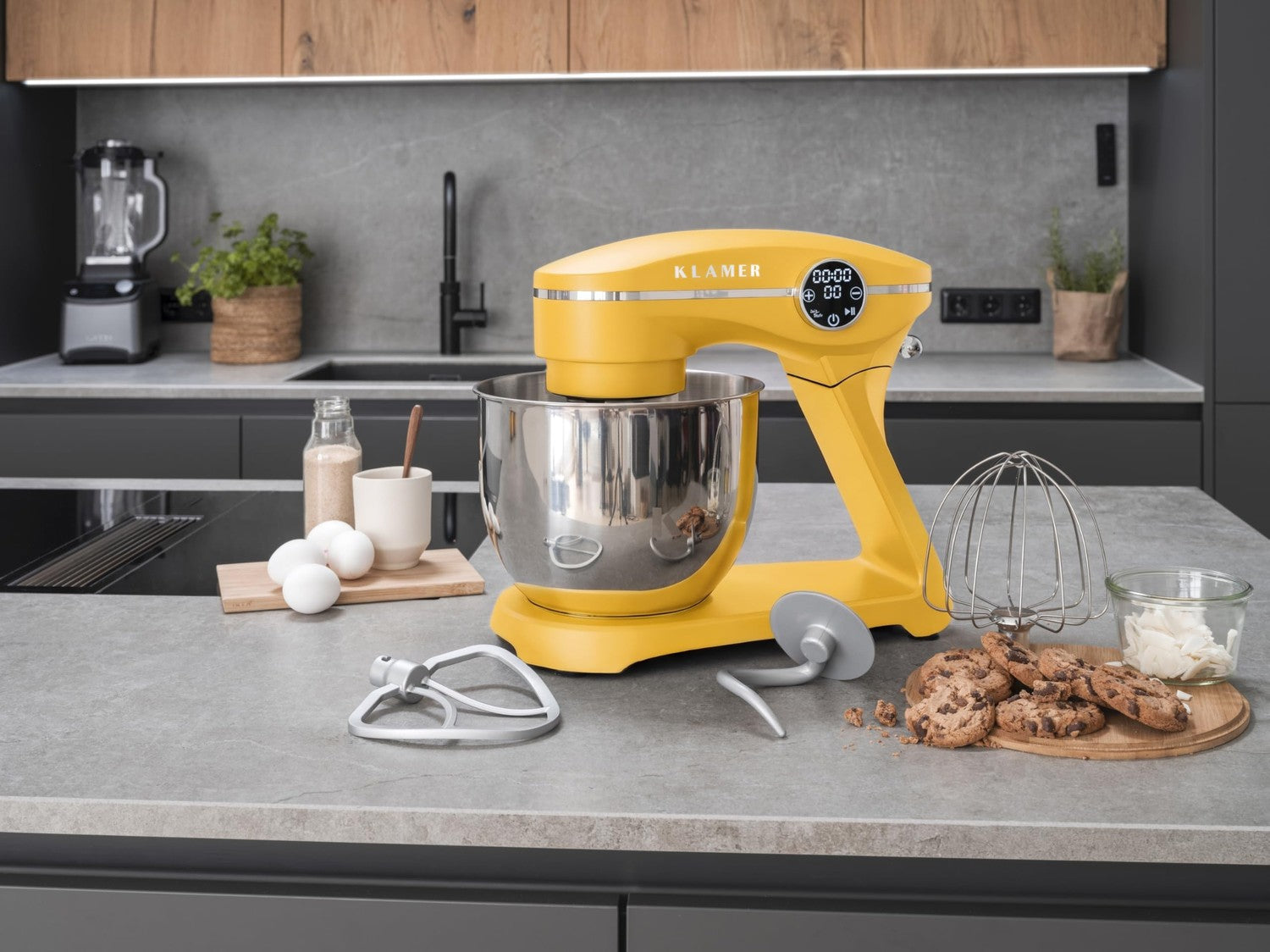 Gelbe Standmixer auf Küchenarbeitsplatte mit Rührbesen, Teig, Eiern und Keksen.