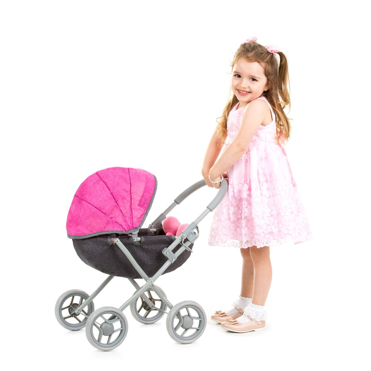 Ein kleines Mädchen im rosa Kleid schiebt einen Spielzeug-Kinderwagen.