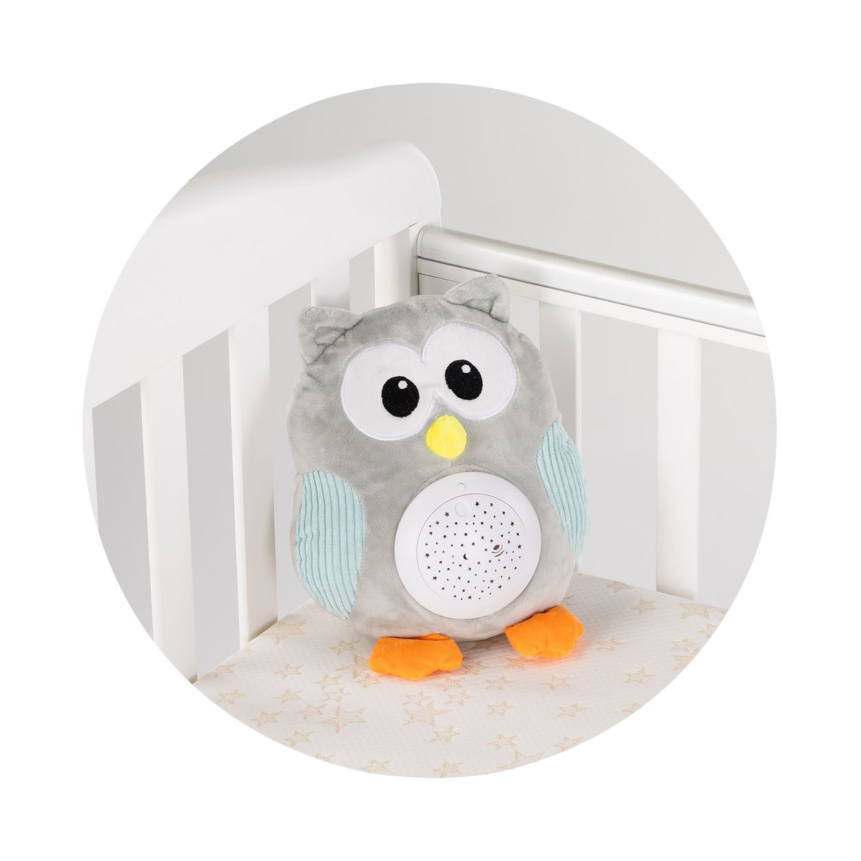 Ein graues und weißes Plüsch-Eulenspielzeug mit Sternprojektor auf dem Bauch sitzt in einem weißen Babybett.
