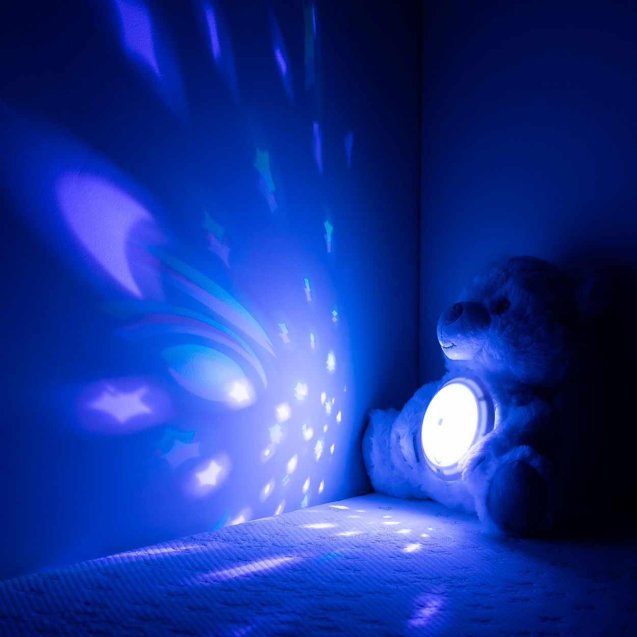 Ein Plüschteddybär mit leuchtendem Bauch projiziert blaue Sterne an eine dunkle Wand.