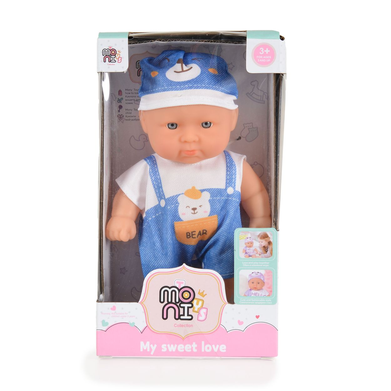 Eine Babypuppe mit blauem Bärenhut und Latzhose in einer rosa-weißen Spielzeugverpackung.