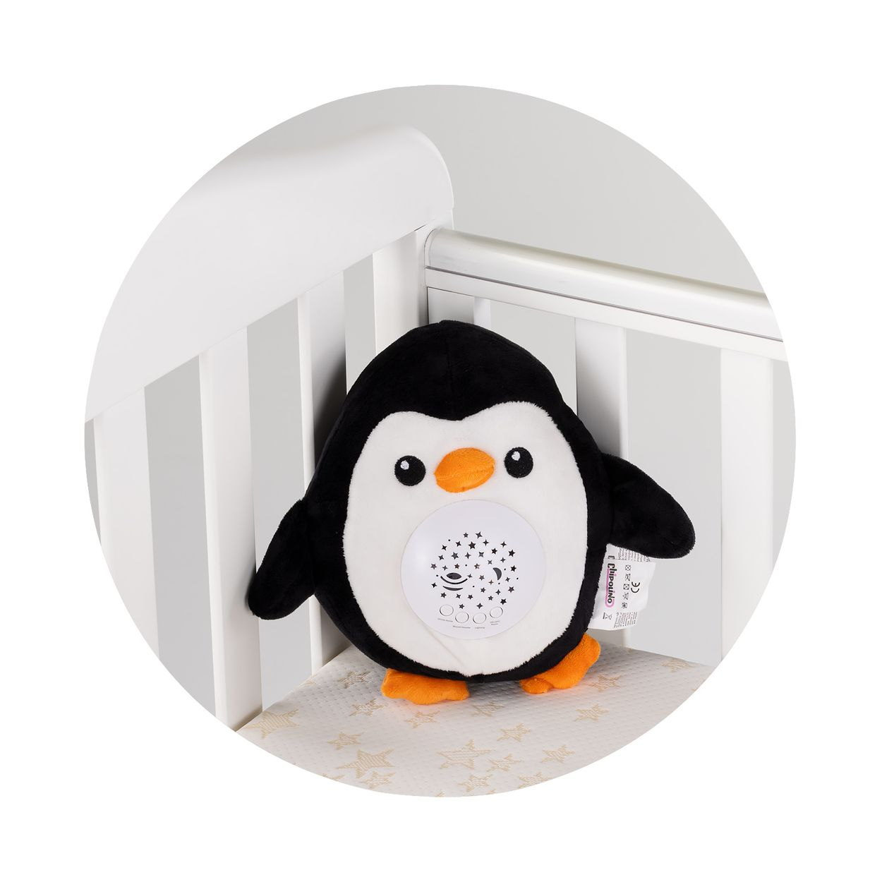 Ein weicher Plüschpinguin mit Sternenprojektor sitzt in einem weißen Kinderbett.
