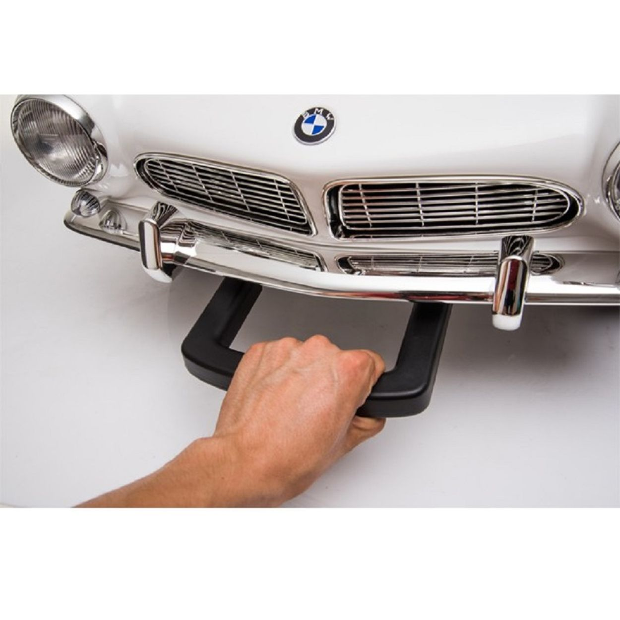 Eine Hand zieht an einem schwarzen Griff an der Vorderseite eines weißen BMW-Spielzeugautos.