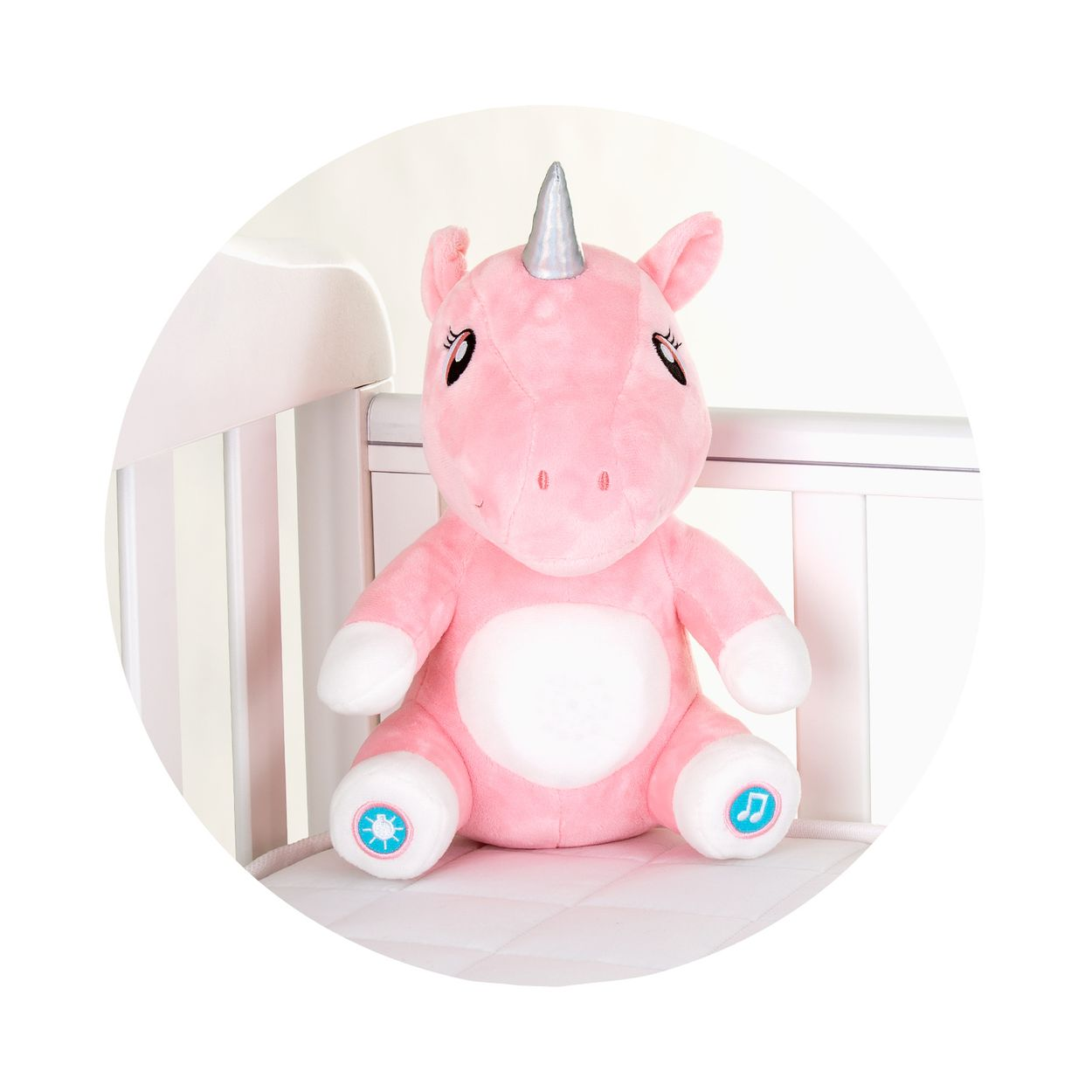 Ein rosa Plüsch-Einhorn mit silbernem Horn und blauen Knöpfen an den Füßen sitzt in einem weißen Gitterbett.