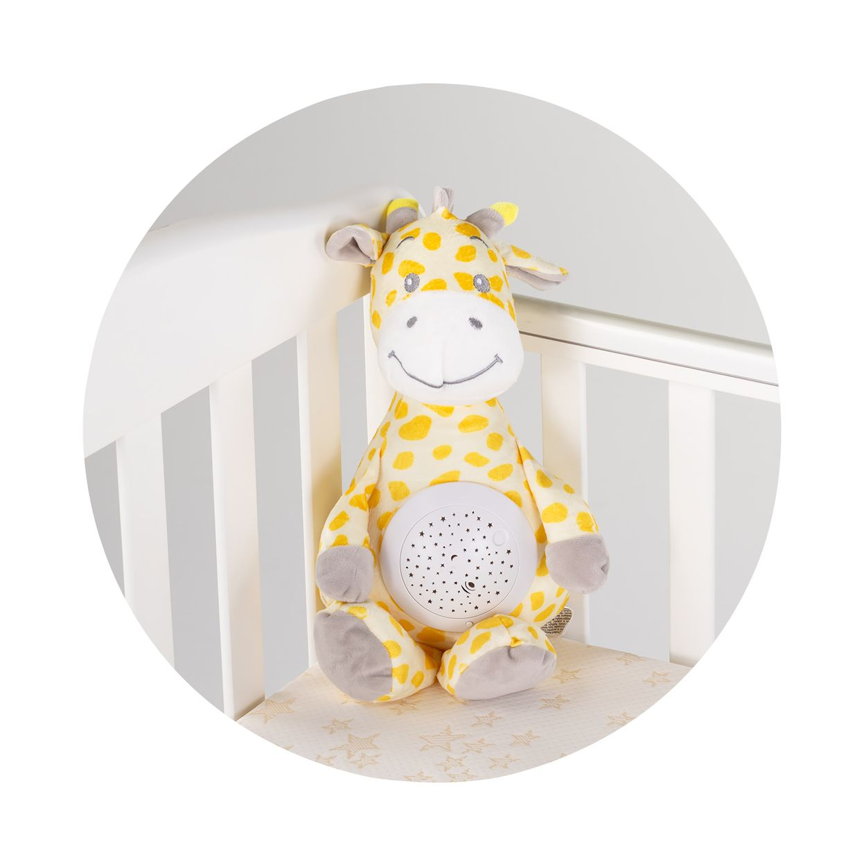 Eine plüschige gelb-weiße Giraffe mit einem weißen Projektor auf dem Bauch sitzt in einem weißen Gitterbett.