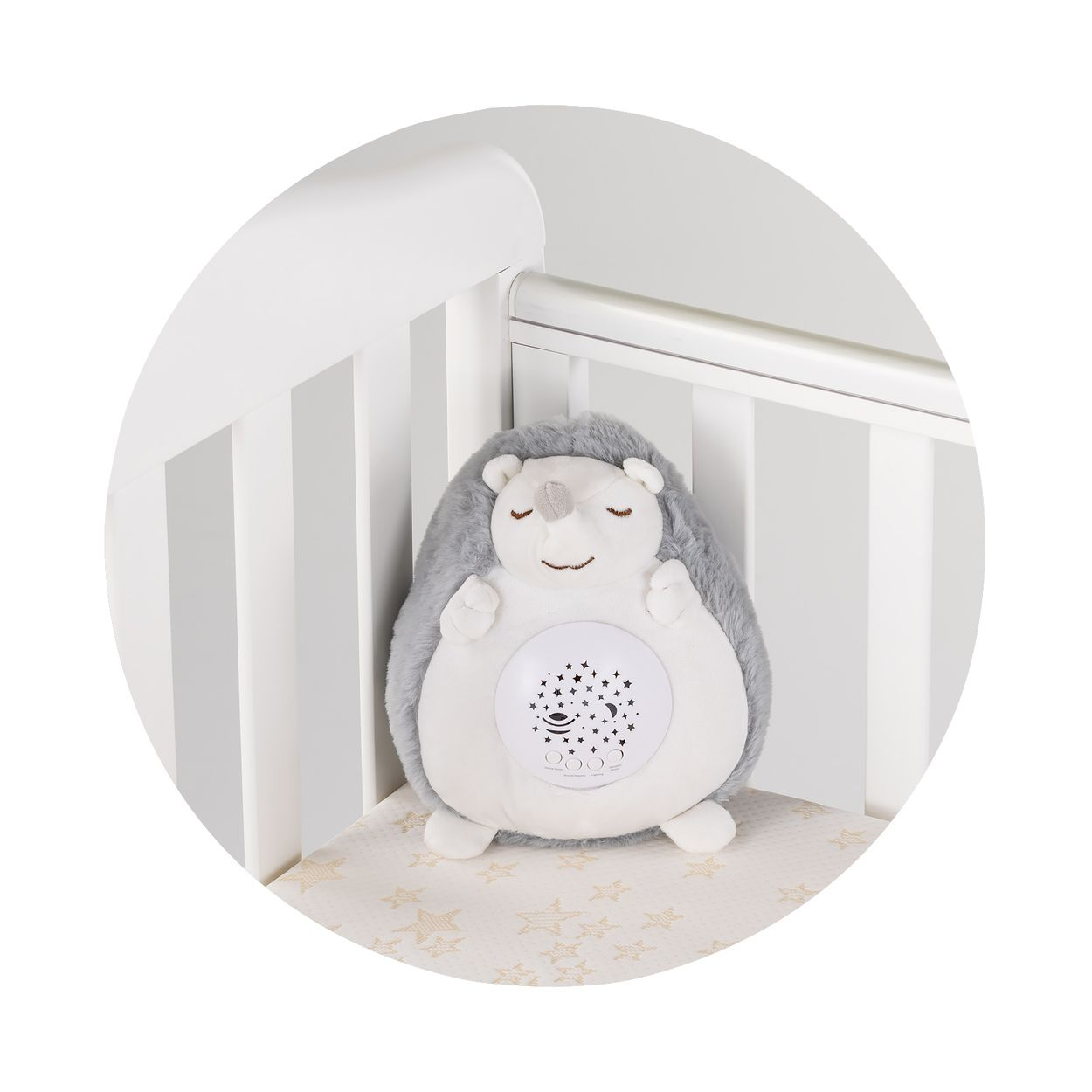 Ein grauer Plüschigel mit einem Sternenprojektor auf dem Bauch sitzt in einem weißen Kinderbett.