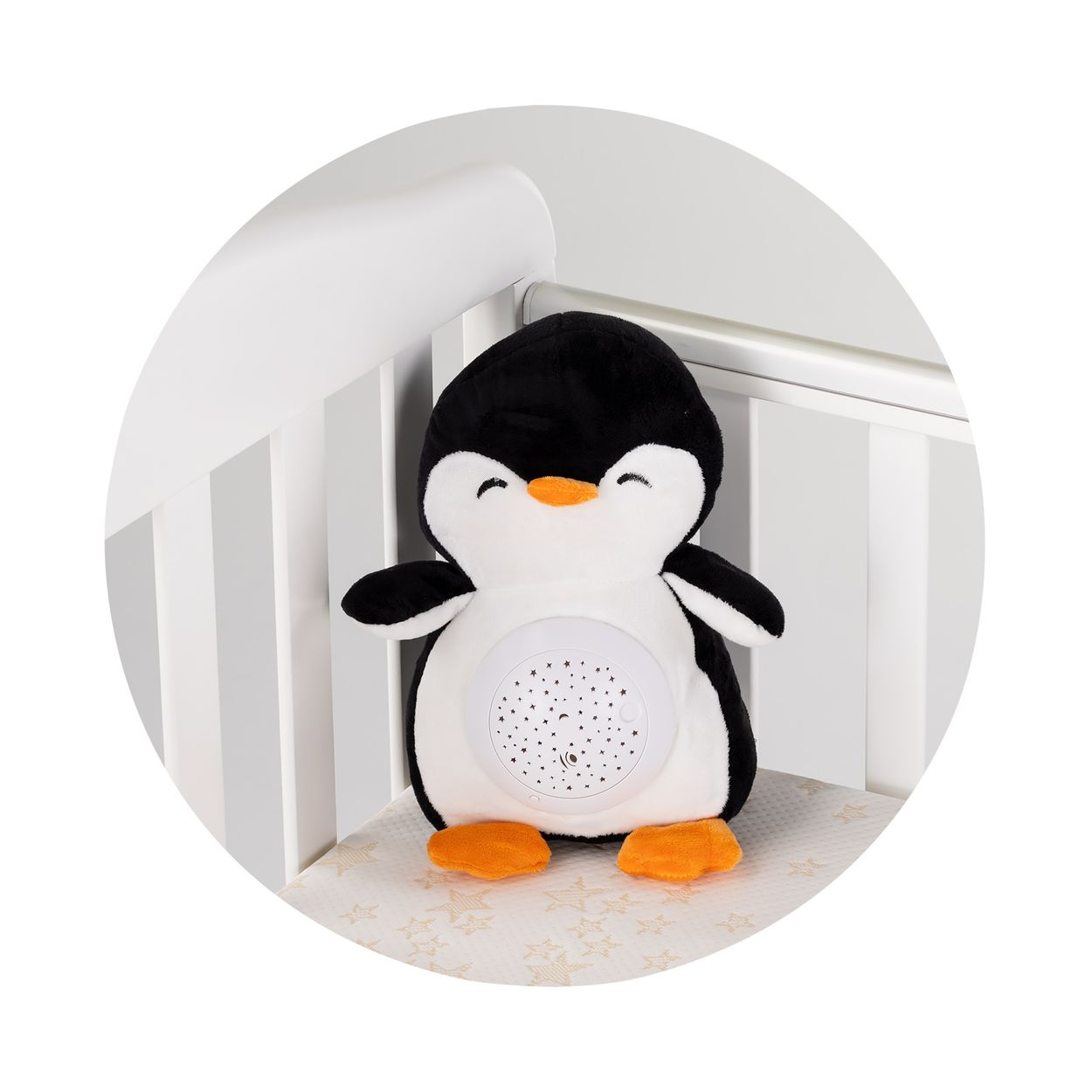 Ein schwarz-weißer Plüschpinguin mit Projektor auf dem Bauch sitzt in einem weißen Kinderbett.