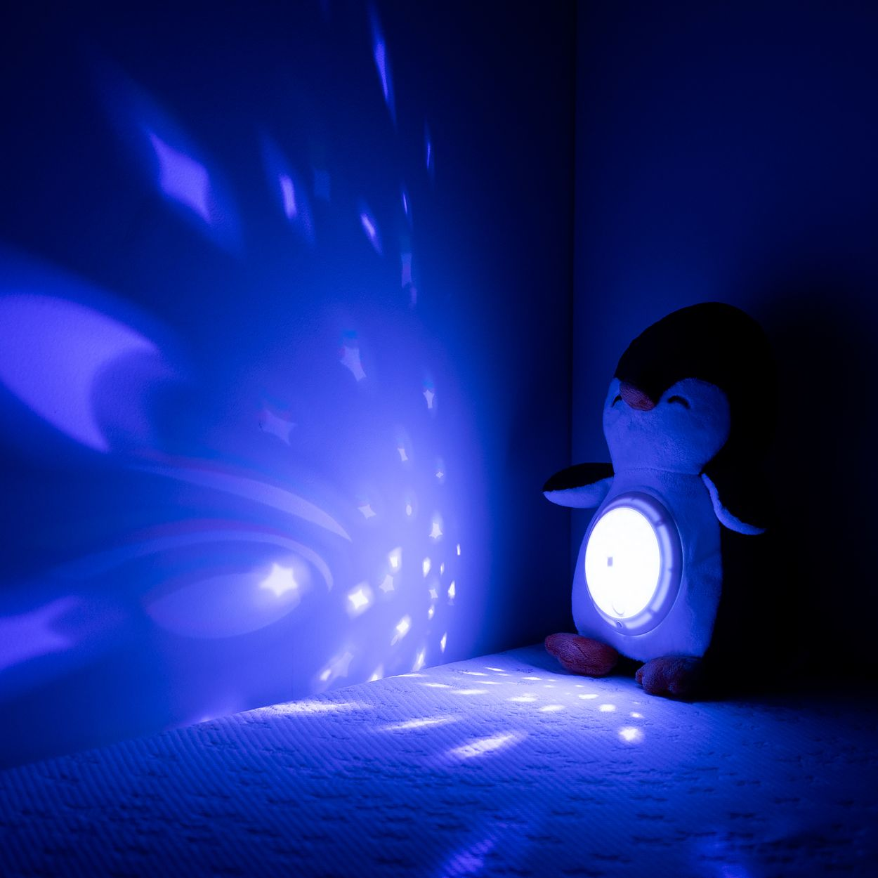 Ein Kuschelpinguin mit eingebautem Nachtlicht projiziert blaue Sterne an die Wand.