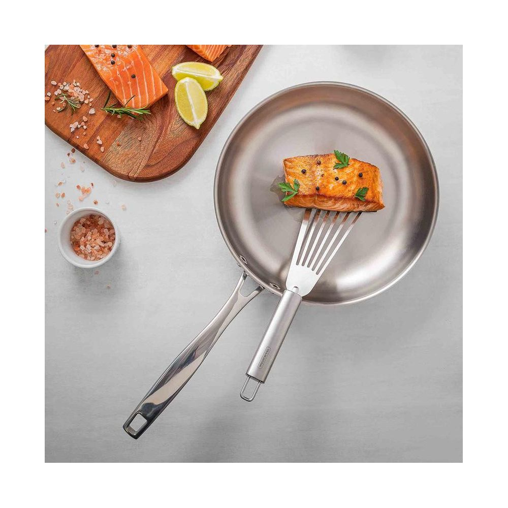 Filet de saumon soulevé dans une poêle en inox avec une spatule, à côté de saumon et de citrons verts.