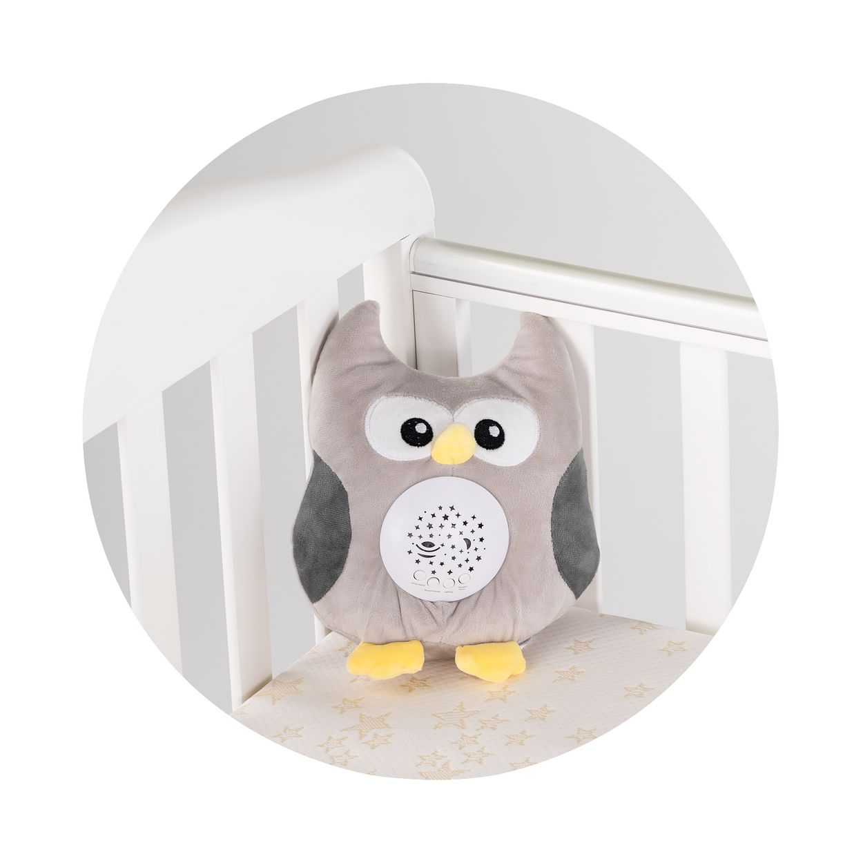 Eine graue Plüsch-Eule mit gelbem Schnabel und Sternenprojektor auf dem Bauch sitzt in einem weißen Babybett.