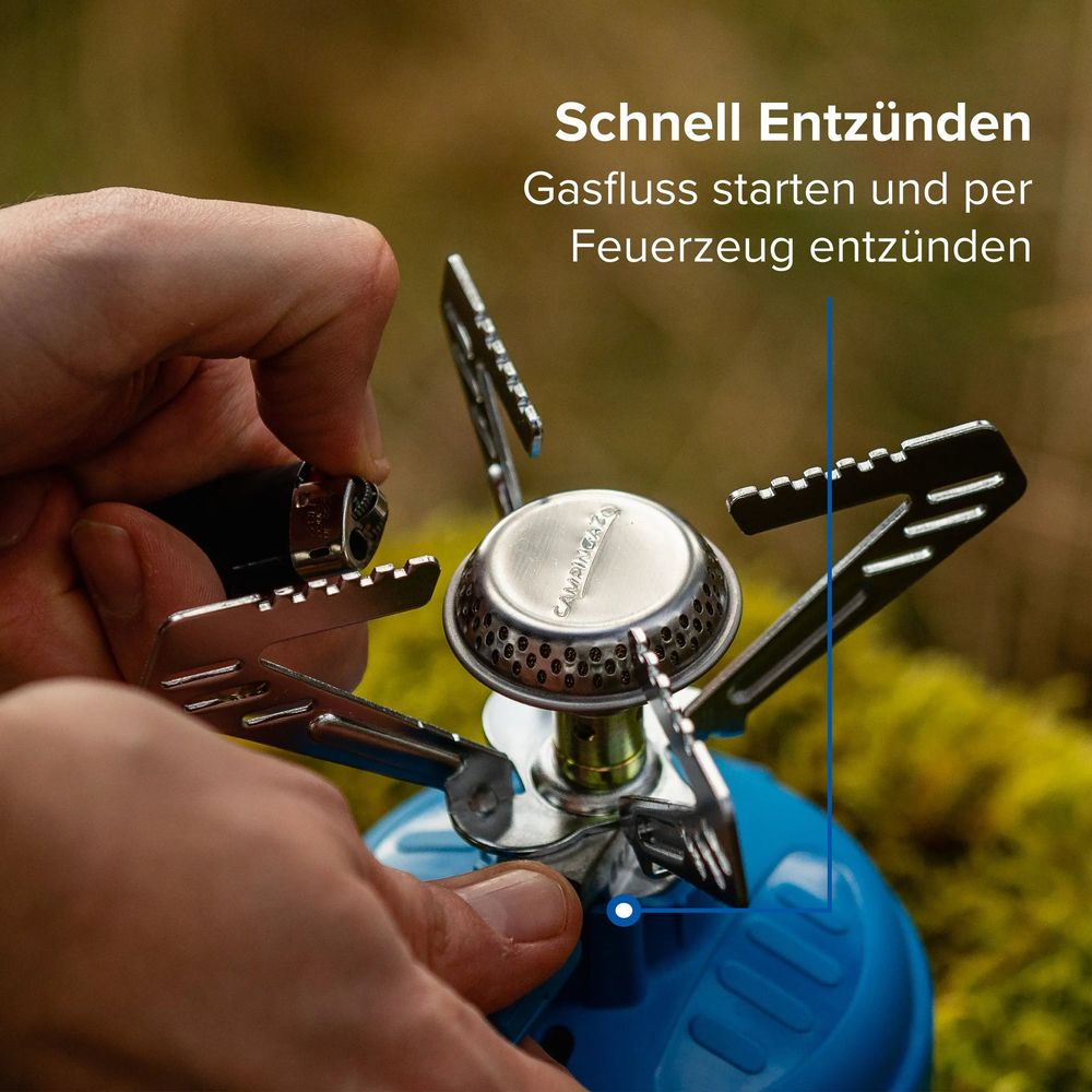 Eine Person entzündet draußen einen tragbaren Gaskocher auf einer blauen Gaskartusche.