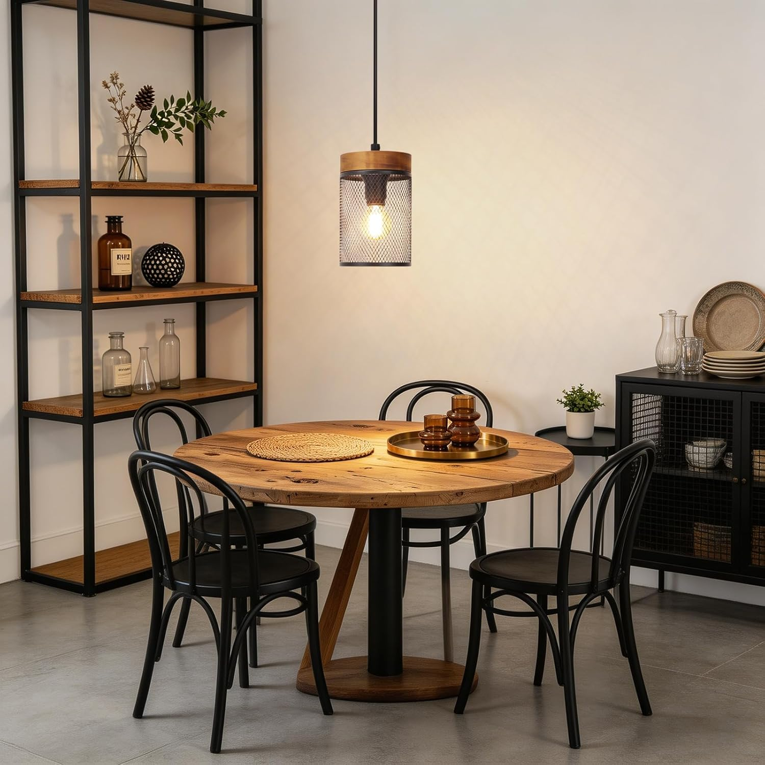 Ein runder Holzesstisch mit vier schwarzen Stühlen, einer hängenden Gitterlampe und einem hohen Regal links.