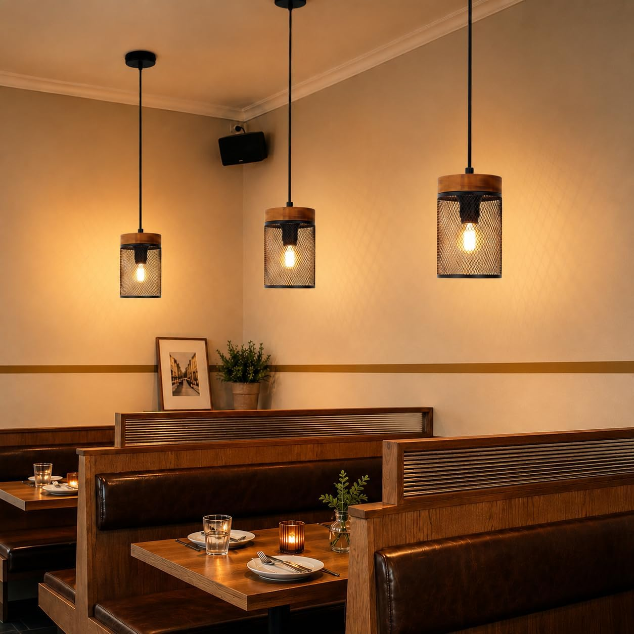 Drei Pendelleuchten hängen über Holzsitzbänken in einem Restaurant und werfen warmes Licht auf Tische mit Gläsern.