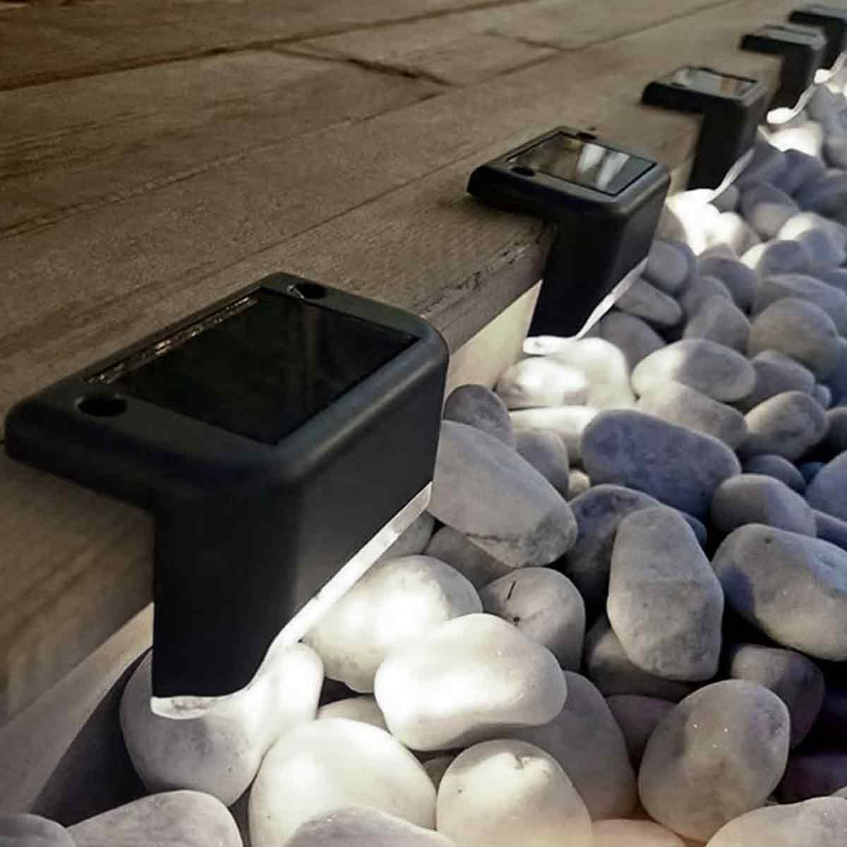 Schwarze Solar-Stufenlichter an einer Holzterrasse über grauen Kieselsteinen.