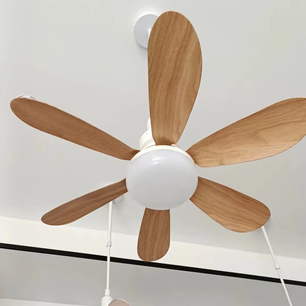 Ein weißer Deckenventilator mit sechs Holzflügeln und einer runden Lampe in der Mitte ist an einer weißen Decke montiert.