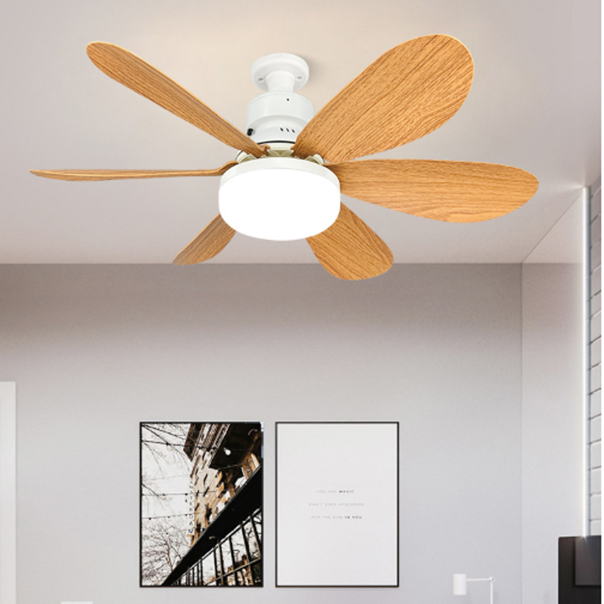 Deckenventilator mit Holzflügeln und integrierter Lampe in einem hellen Zimmer mit zwei Wandbildern.