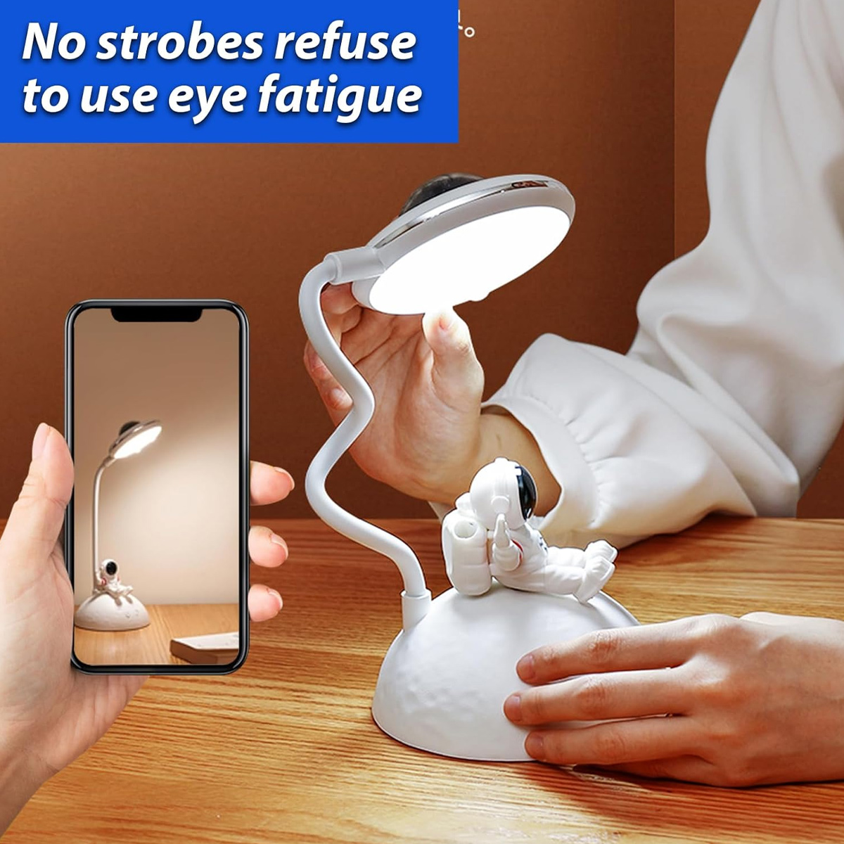 Eine Hand hält ein Smartphone, das eine Astronauten-Schreibtischlampe auf Holzoberfläche fotografiert.
