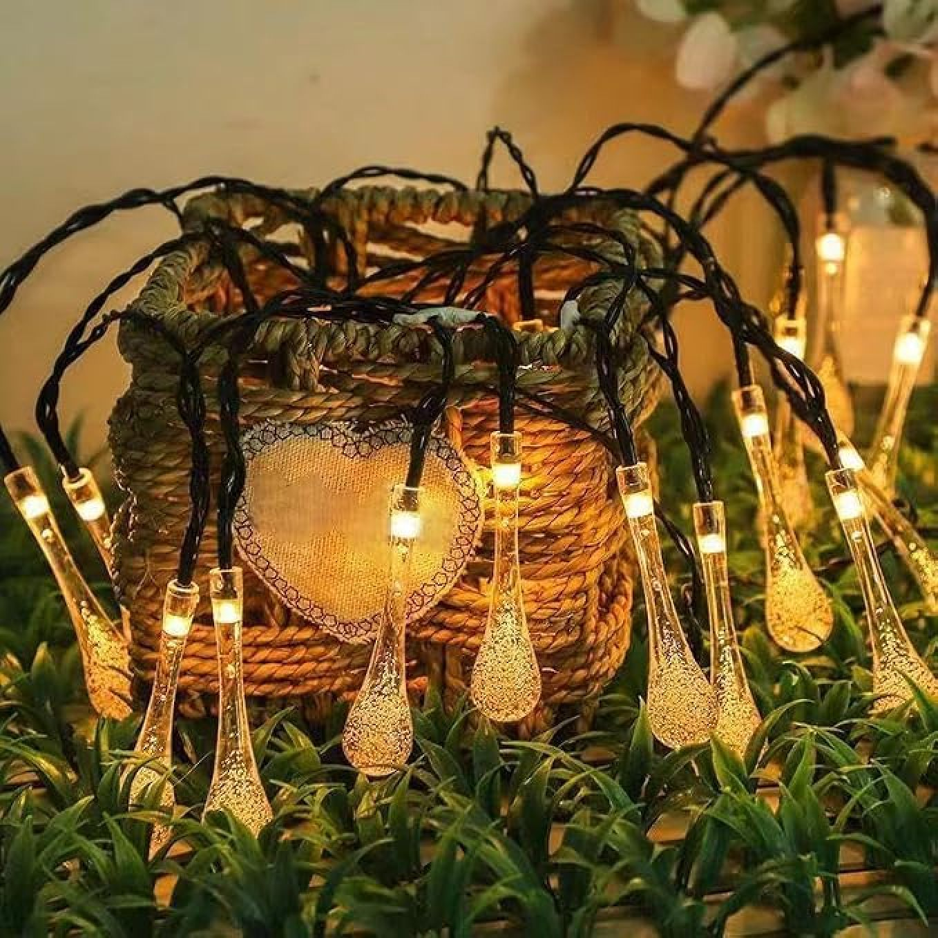 Lichterkette mit tropfenförmigen LEDs, drapiert über einem geflochtenen Korb und künstlichem Grün.