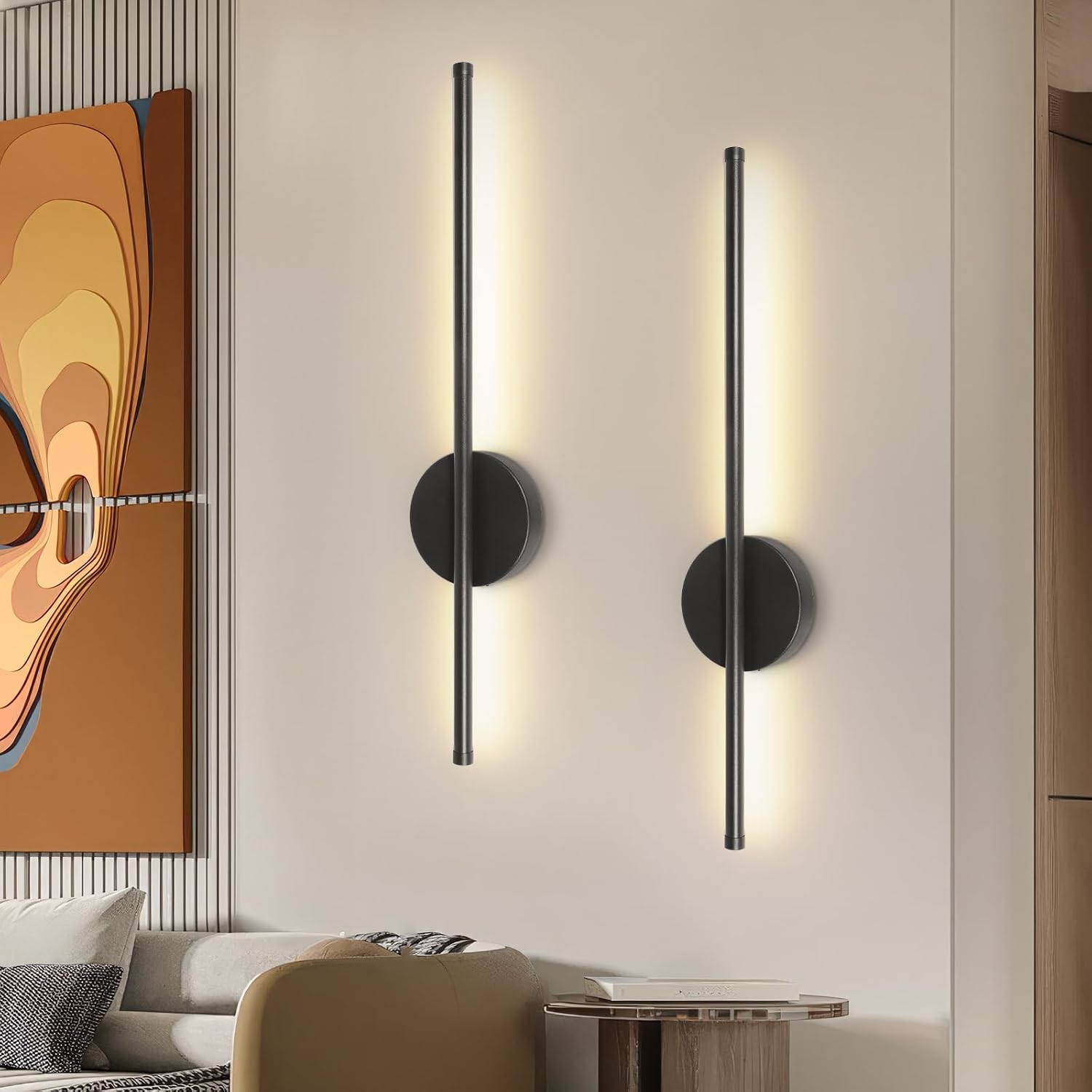 Zwei schwarze vertikale Wandleuchten mit warmem Licht an einer Wand, neben Kunst und Sofa.