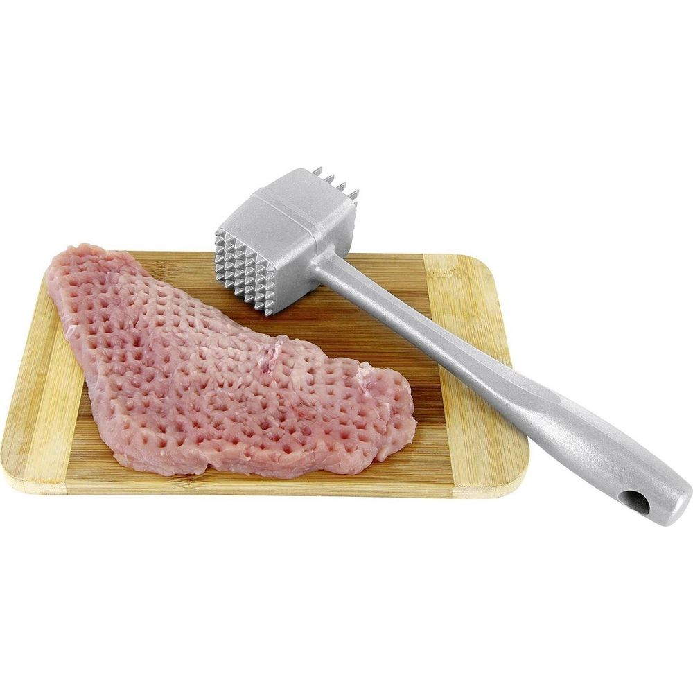 Ein Fleischklopfer aus Metall liegt neben rohem Fleisch auf einem Holzschneidebrett vor weißem Hintergrund.