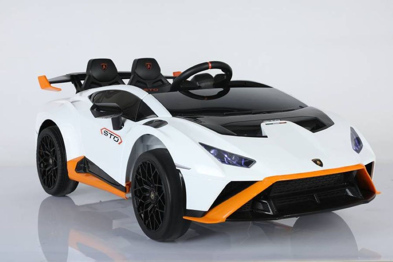 Ein weiß-oranges Lamborghini-Kinder-Elektroauto mit schwarzen Felgen und Sitzen auf weißem Grund.
