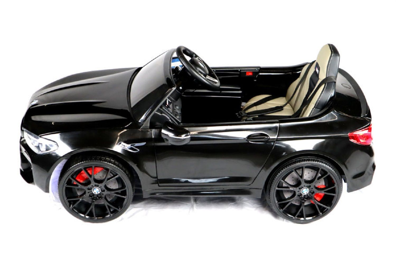 Ein schwarzes Kinder-Elektroauto in Seitenansicht mit roteren Bremssätteln und hellem Ledersitz vor weißem Hintergrund.
