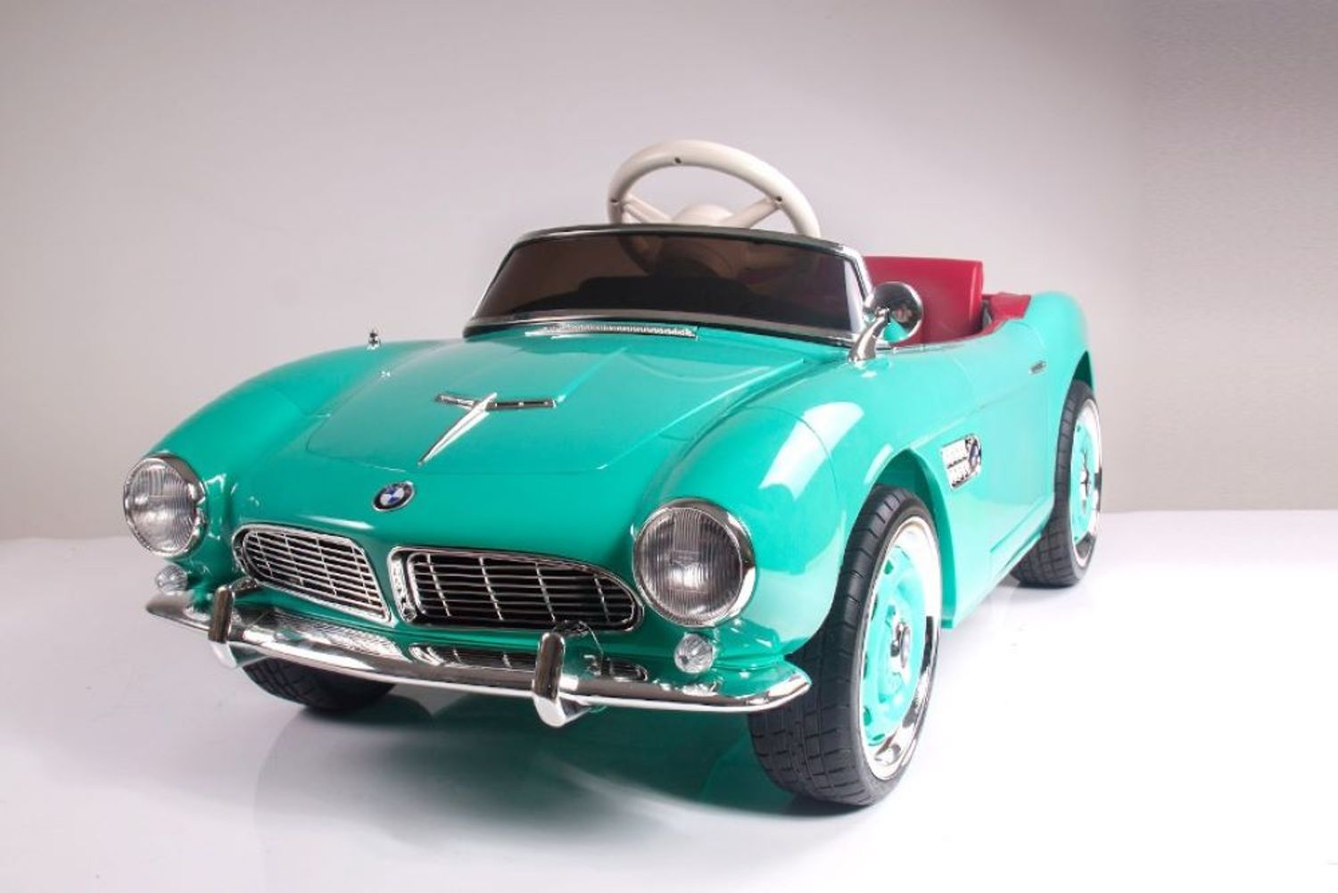 Ein türkisfarbenes Retro-Kinderauto mit rotem Interieur auf weißem Grund.