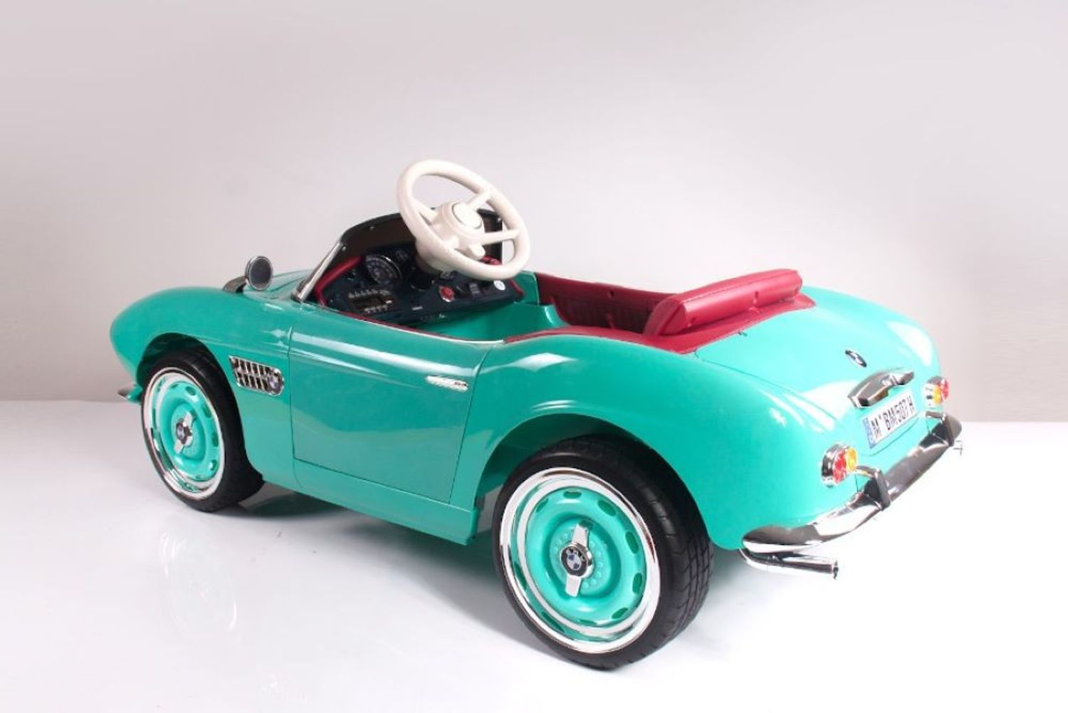 Ein türkisfarbenes Spielzeugauto mit roten Sitzen und einem weißen Lenkrad auf hellem Hintergrund.