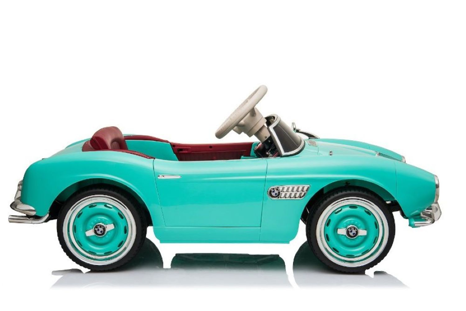 Ein türkisfarbenes Retro-Kinderauto mit rotem Ledersitz und weißem Lenkrad auf weißem Hintergrund.