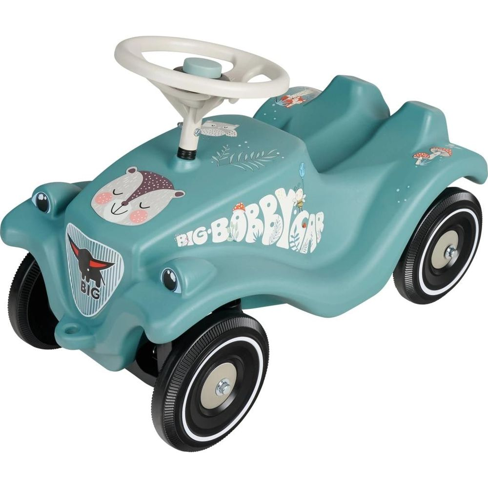 Ein mattgrünes Bobby-Car mit weißem Lenkrad, Tieren und Pilzen verziert, steht auf weißem Grund.