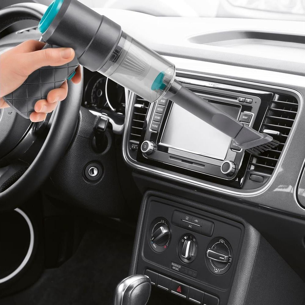 Hand hält einen kleinen Staubsauger, der das Armaturenbrett eines Autos reinigt.