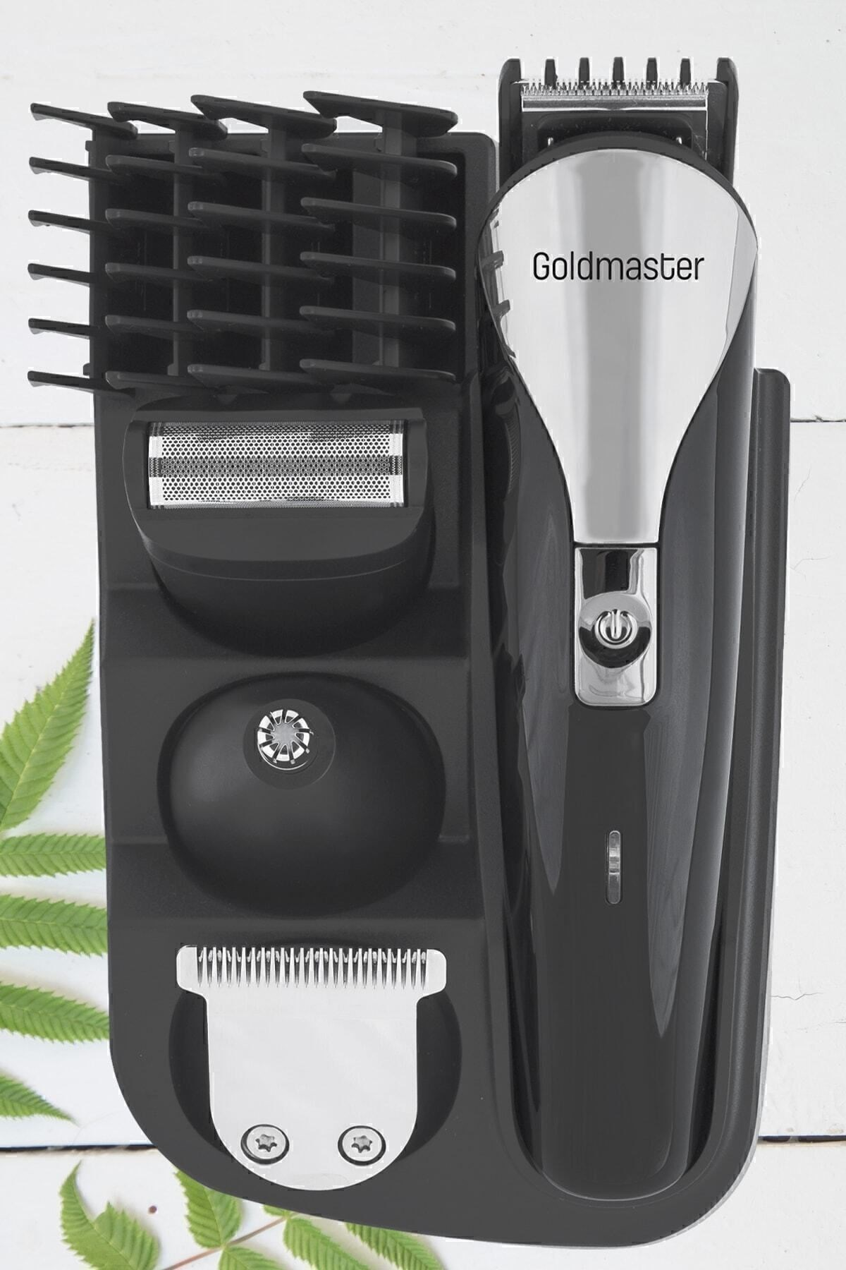 Goldmaster saç kesme makinesi seti, stant üstünde ataçmanlarla, beyaz ve yeşil yaprak arka planında.