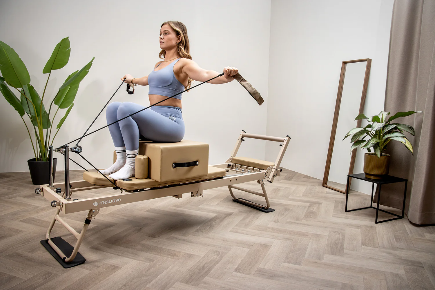Una mujer con ropa deportiva azul hace ejercicio en una máquina de pilates con cuerdas en una habitación luminosa.