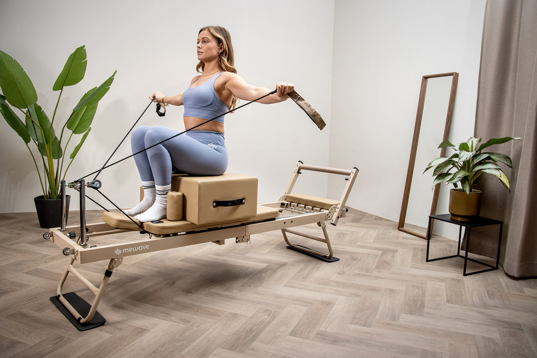 Una mujer con ropa deportiva azul está sentada en una máquina de pilates reformer, tirando de las correas.